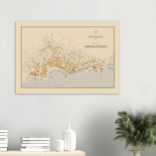 Hamar map print from 1902 displayed on a light grey wall above books and white vases, with a leafy plant beside it.
