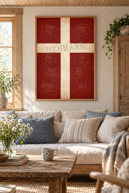 Danish sayings poster displayed on a light grey wall above books and white vases, beside a leafy plant.