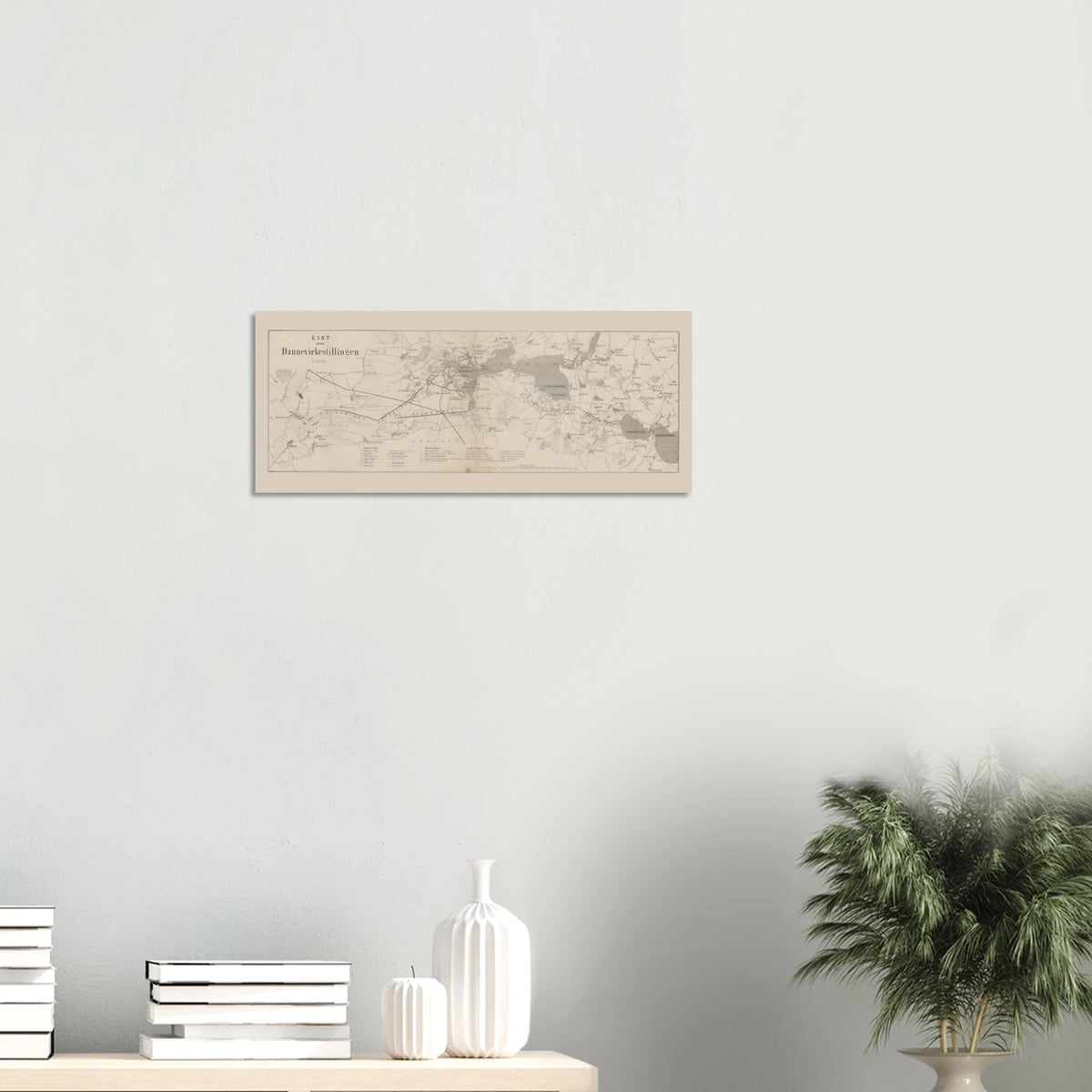 Dannevirke map print displayed horizontally on a light wall above books and white vases, with a leafy plant to the right.