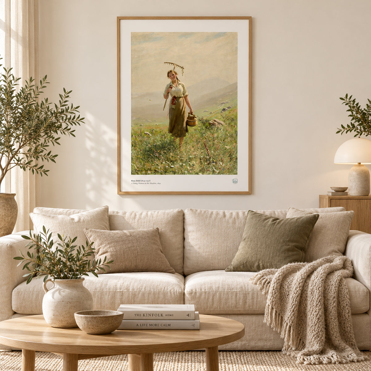 Hans Dahl’s A Young Woman in the Meadow (1894) poster with white border, displayed above books and white ceramics beside a plant.